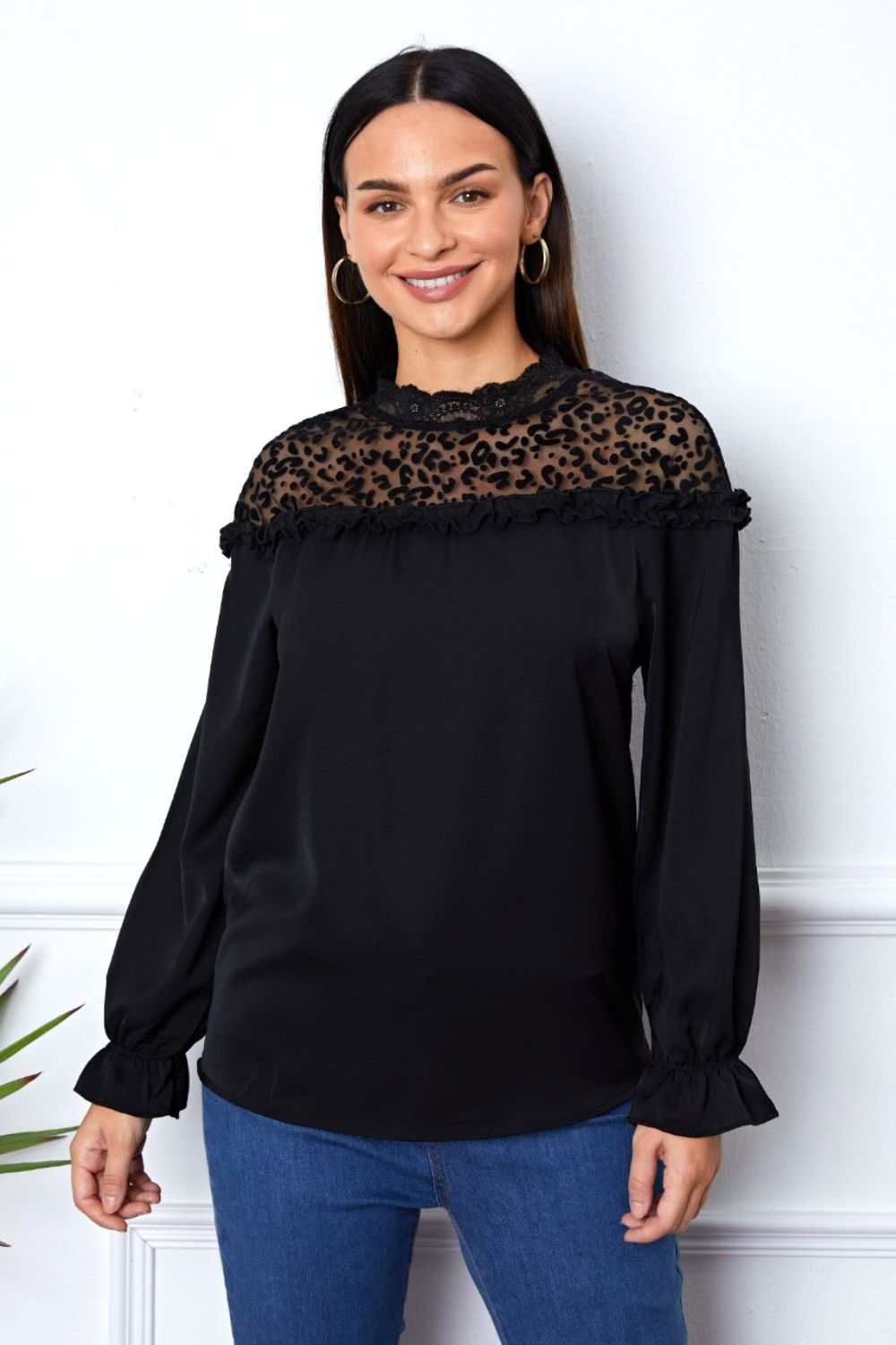 Woman wearing a black leopard frill flounce sleeve blouse with sheer yoke and long sleeves paired with blue jeans