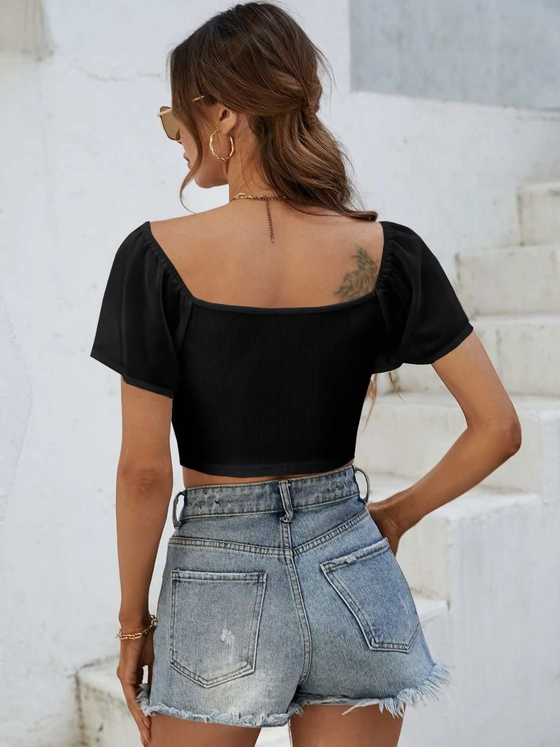 Black drawstring short sleeve crop top with moderate stretch, paired with distressed denim shorts.