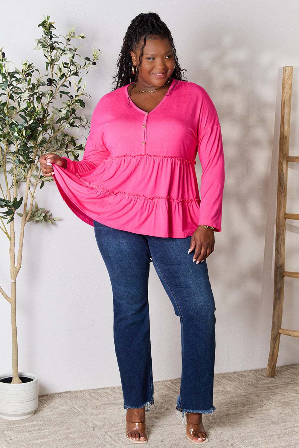 Plus size model wearing pink half button long sleeve ruffle hem blouse with jeans.
