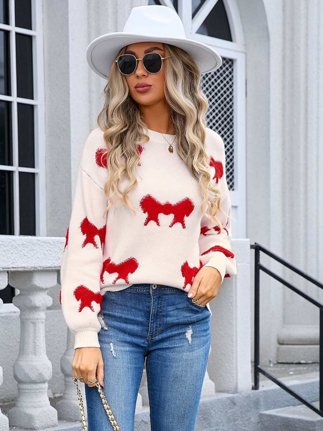 Angel Wings Bow Round Neck Dropped Shoulder Sweater in white with red designs, worn by a model with long blonde hair, sunglasses, and white hat.