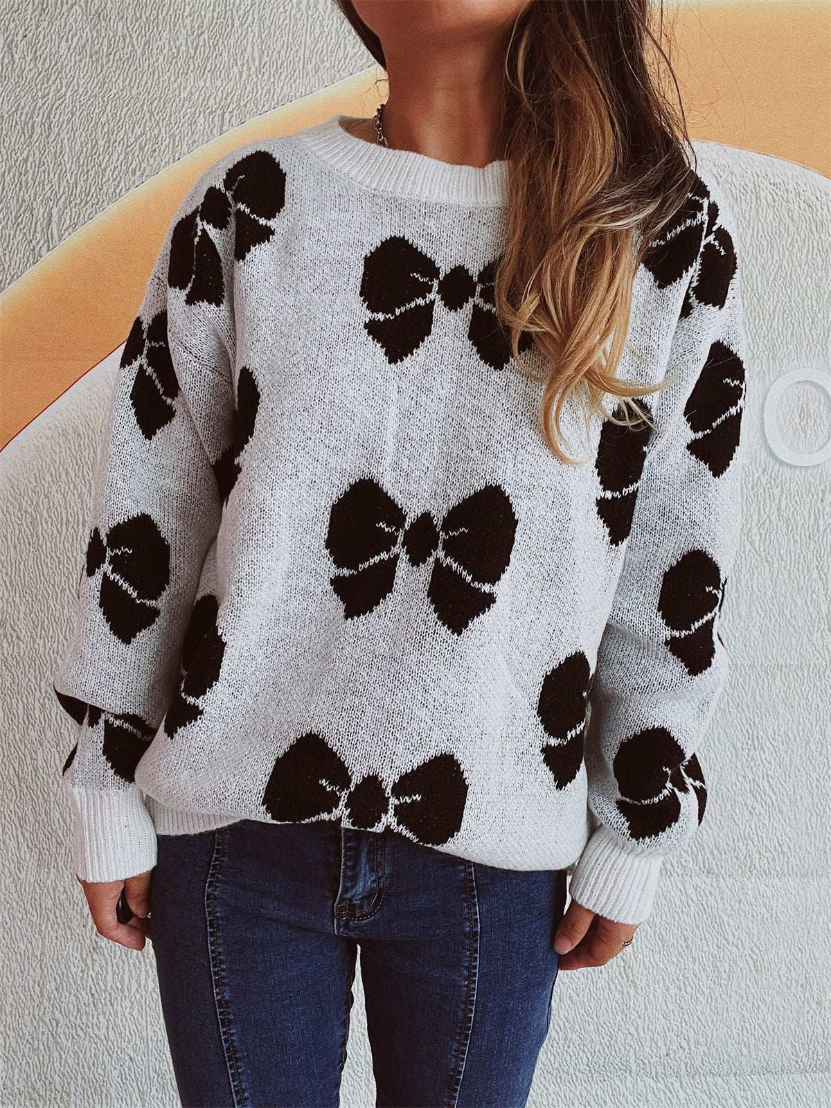 Bow round neck dropped shoulder sweater with black bow patterns on white background.