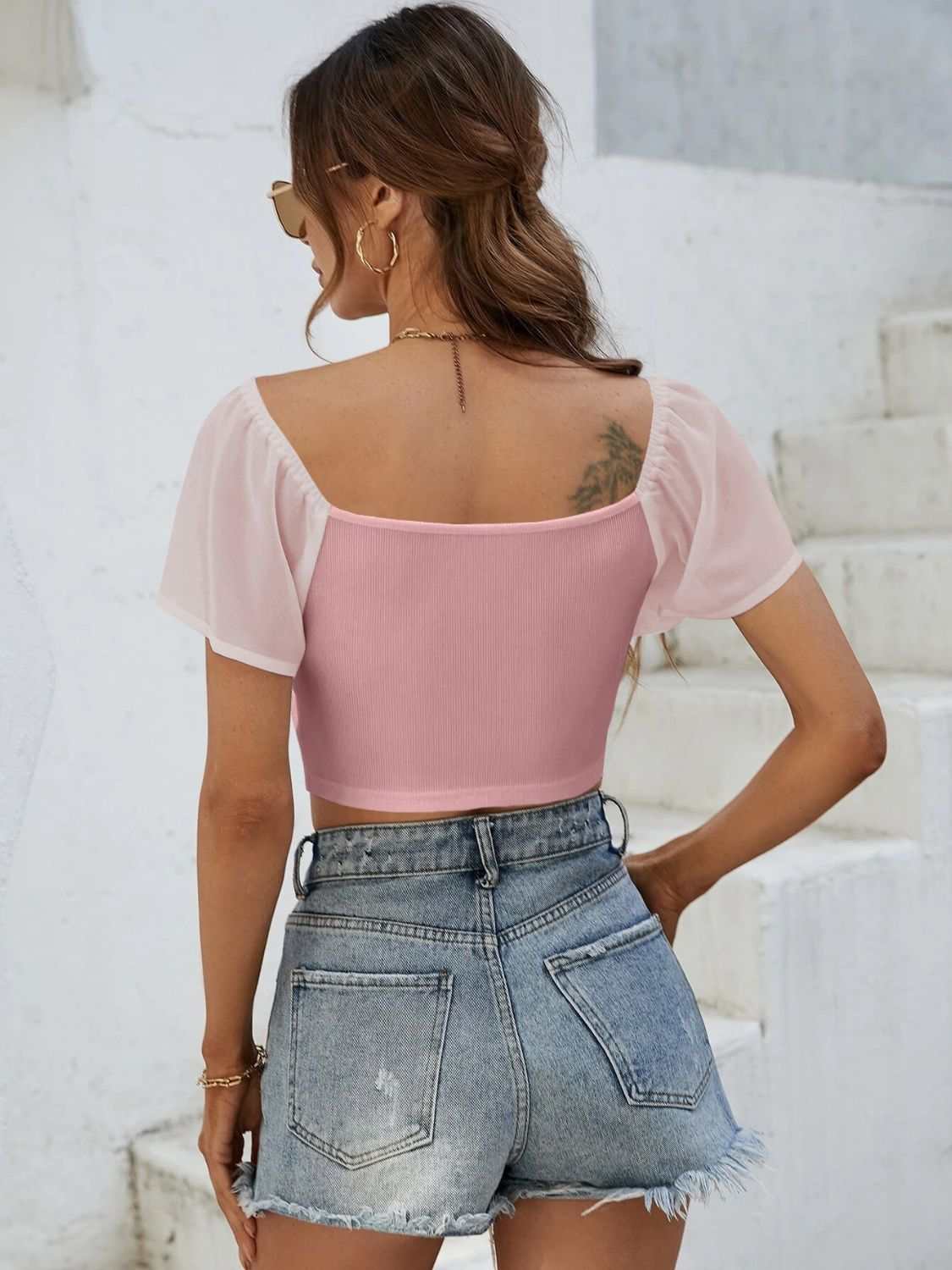 Woman wearing a pink drawstring short sleeve crop top with jeans shorts.