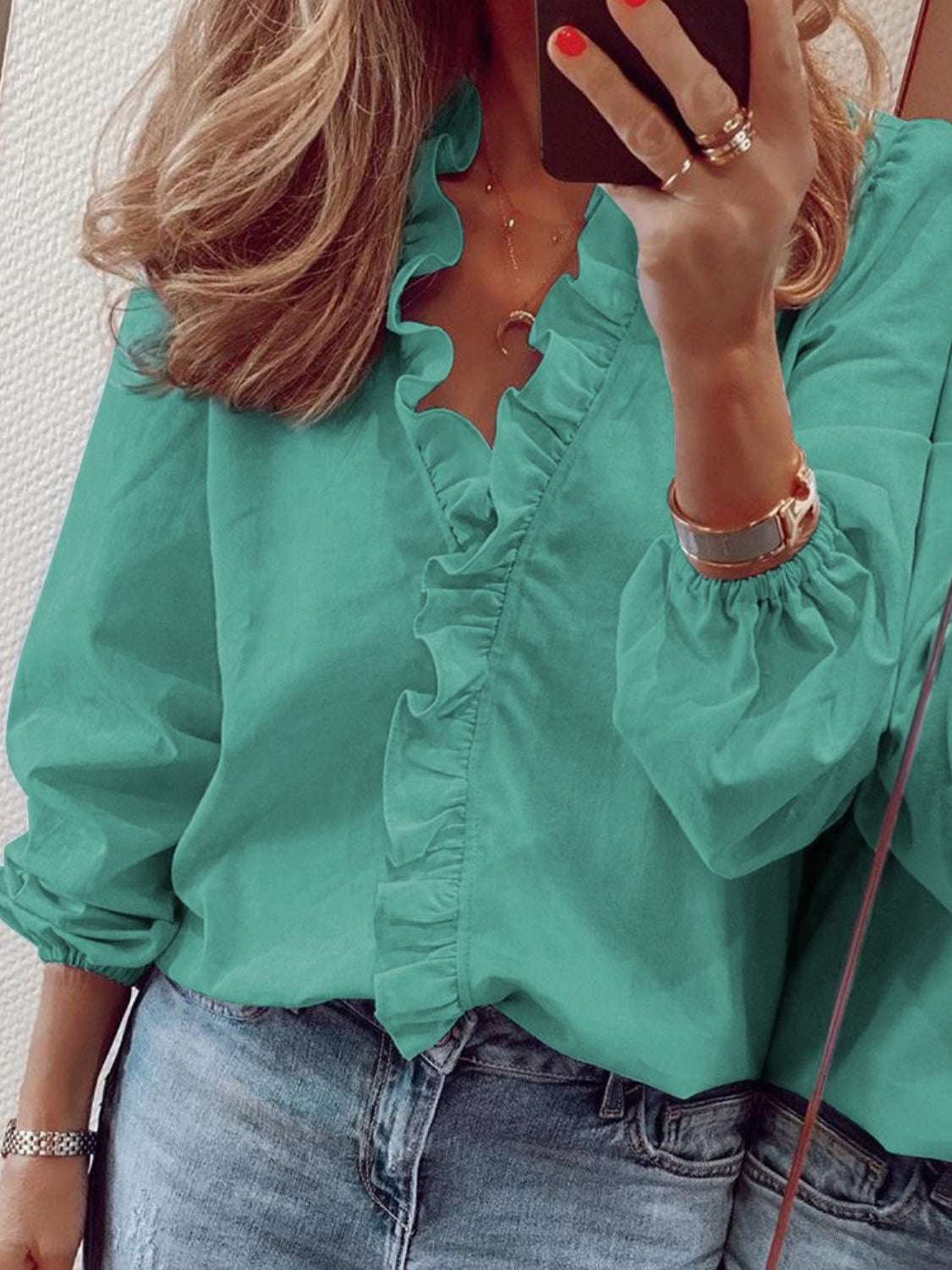 Ruffled V-neck long sleeve blouse in green worn with jeans.