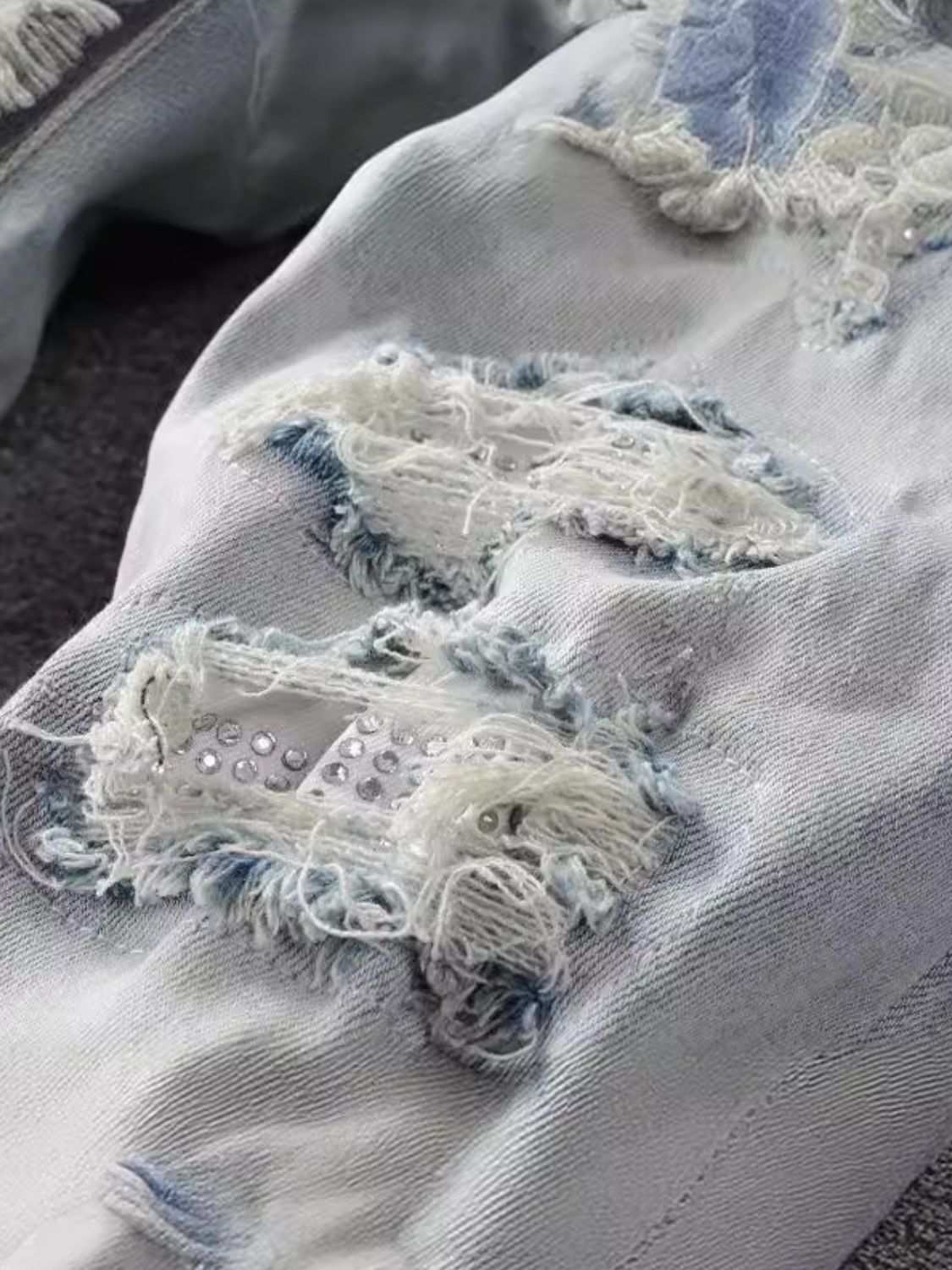 Men's distressed jeans with visible frayed patches and studded details.