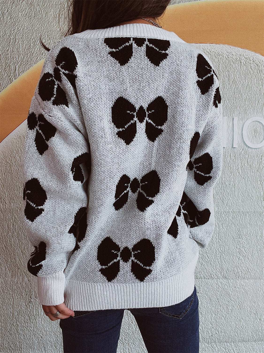 Bow round neck dropped shoulder sweater with black bow patterns on white background, moderate stretch, polyester-acrylic blend.