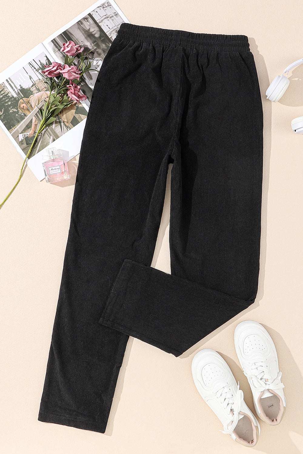 Black drawstring straight pants with pockets, 100% polyester, lying flat with white sneakers nearby.