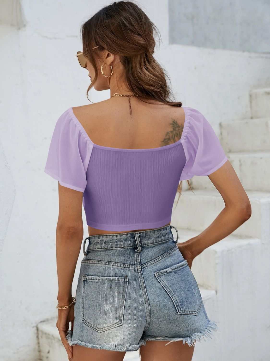 Woman wearing a purple drawstring short sleeve crop top with denim shorts.