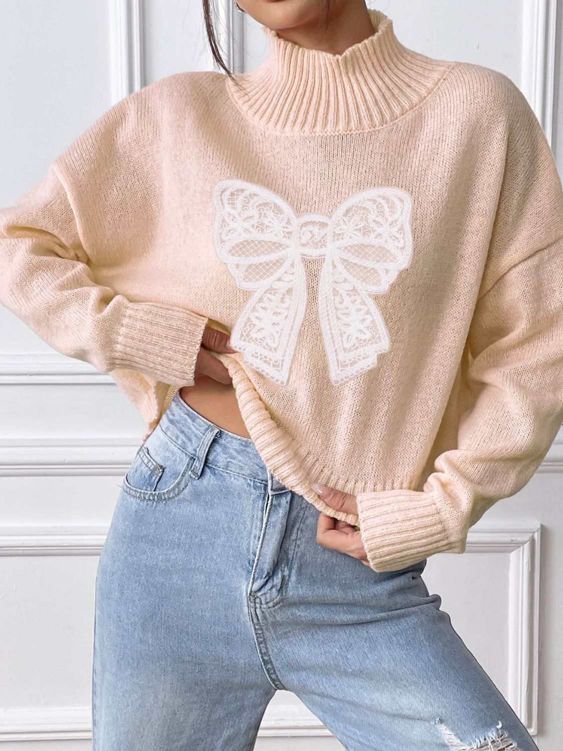 Bow turtleneck long sleeve sweater in beige with white bow design, slightly stretchy, polyester.