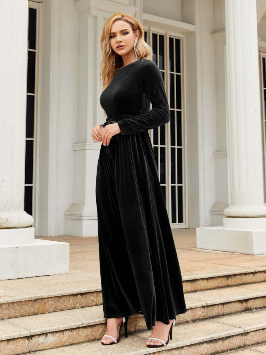 Tie front round neck long sleeve maxi dress in black, made from 100% polyester, worn by a model near a white building.