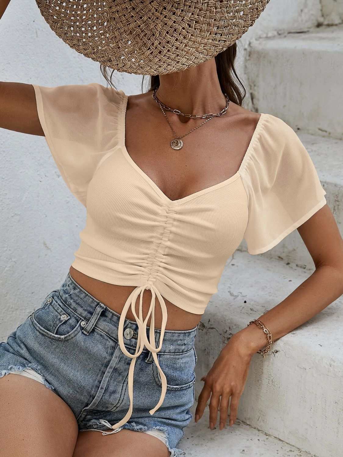 Drawstring short sleeve crop top with moderate stretch and V-neckline, paired with denim shorts.