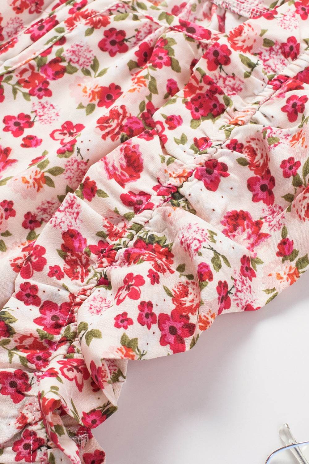 Ruffled floral blouse with cap sleeves and round neck, featuring a pink and red flower pattern.