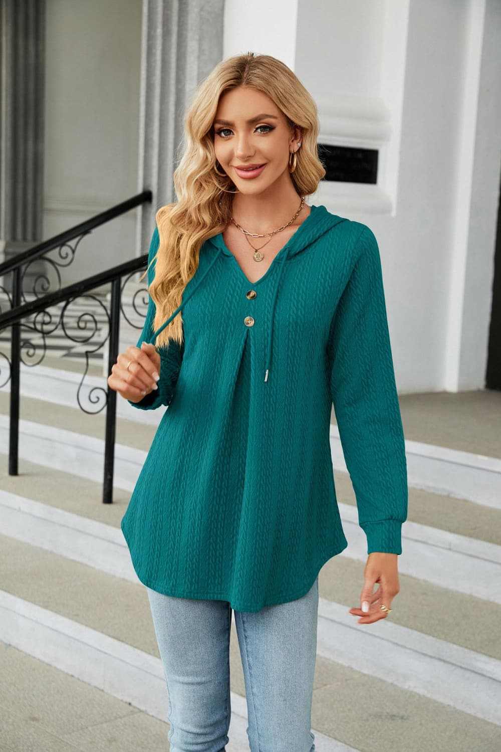 Woman wearing teal long sleeve hooded blouse with drawstring and tie neckline in casual setting