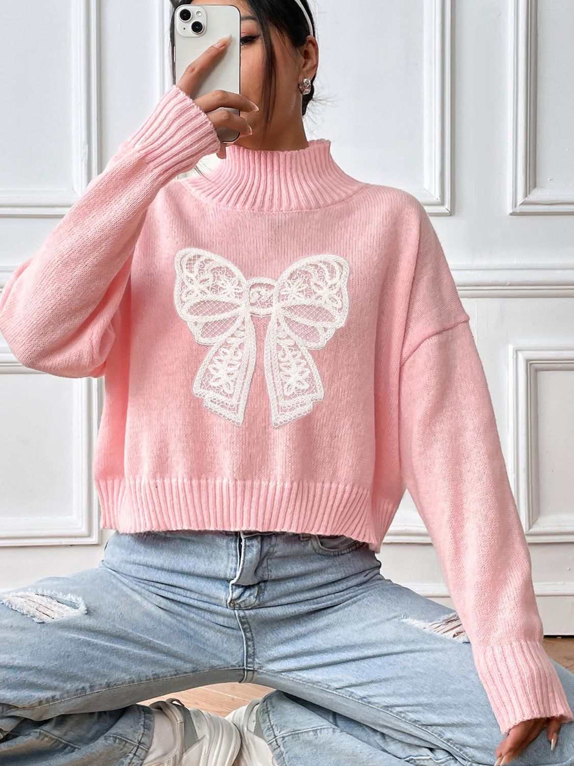 Pink bow turtleneck long sleeve sweater with white lace design, slightly stretchy polyester material.
