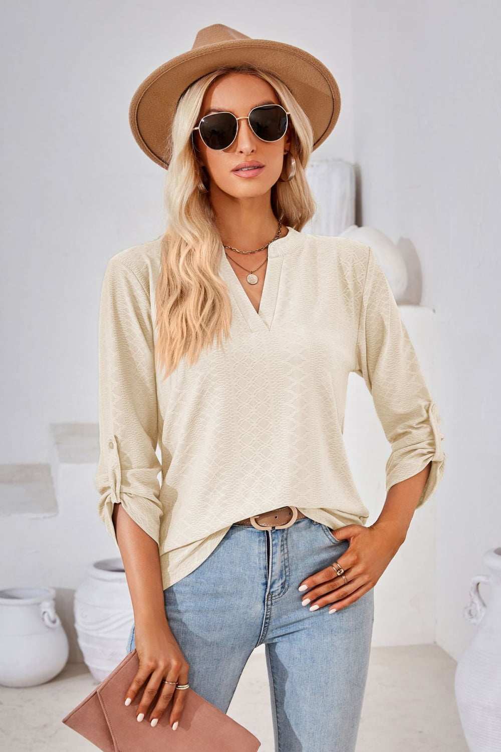 Woman wearing beige V-neck roll-tap sleeve blouse with three-quarter sleeves and light wash jeans