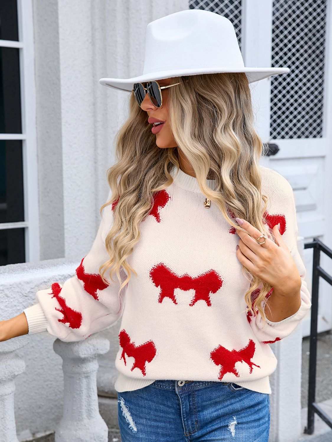 Angel Wings Bow Round Neck Dropped Shoulder Sweater with red patterns and moderate stretch, styled on a model with sunglasses and a white hat.