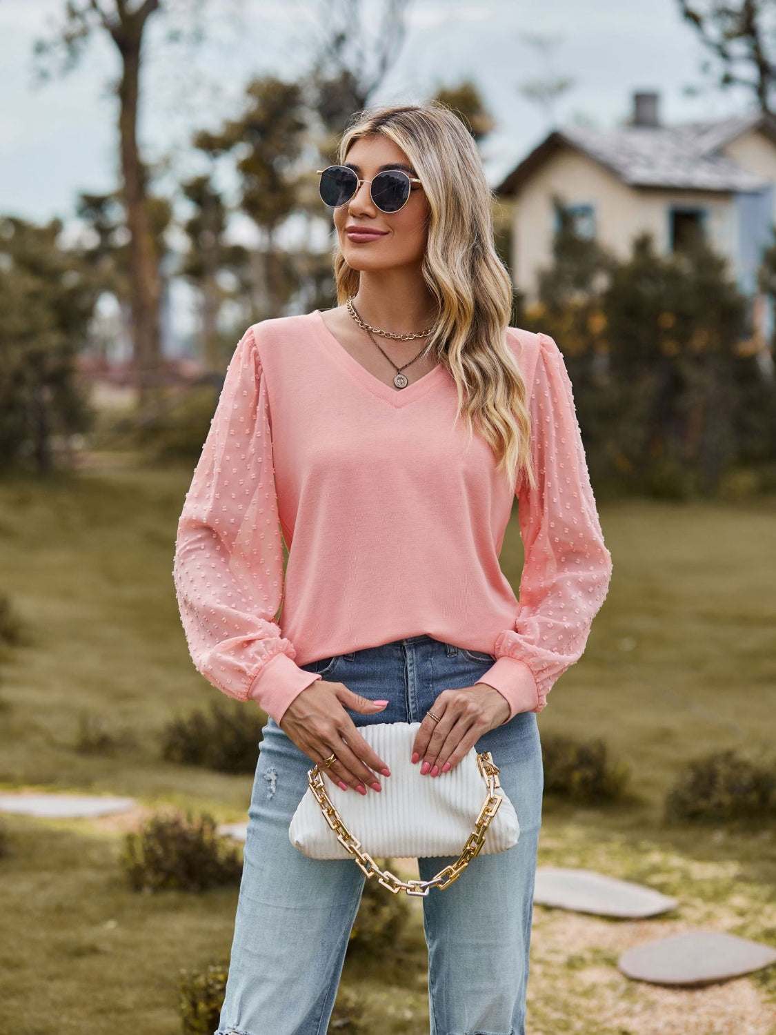 Pink Swiss dot V-neck long sleeve blouse with semi-sheer sleeves and slight stretch, styled with sunglasses and light wash jeans.