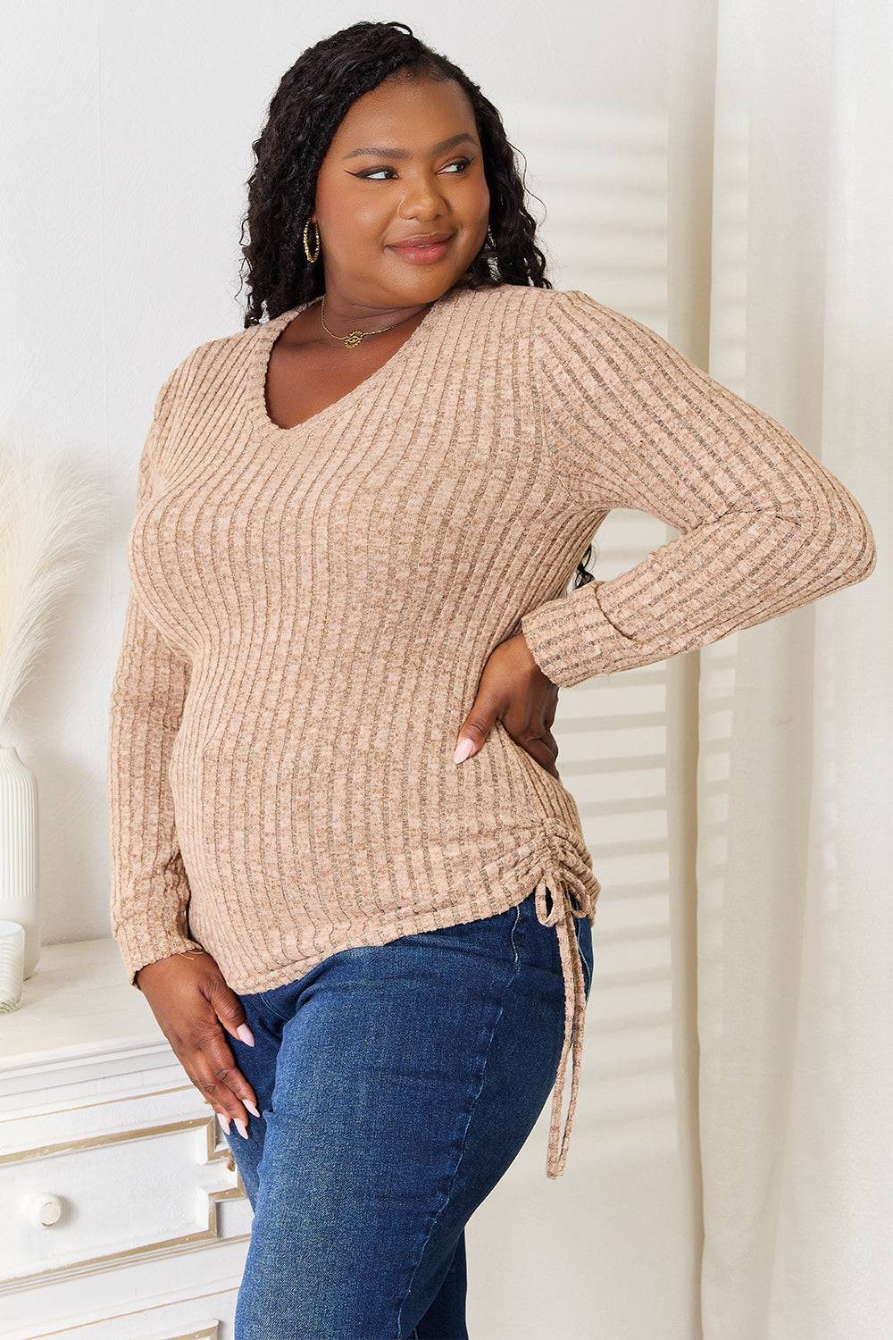 Curvy model wearing a beige drawstring ribbed long sleeve t-shirt with jeans.