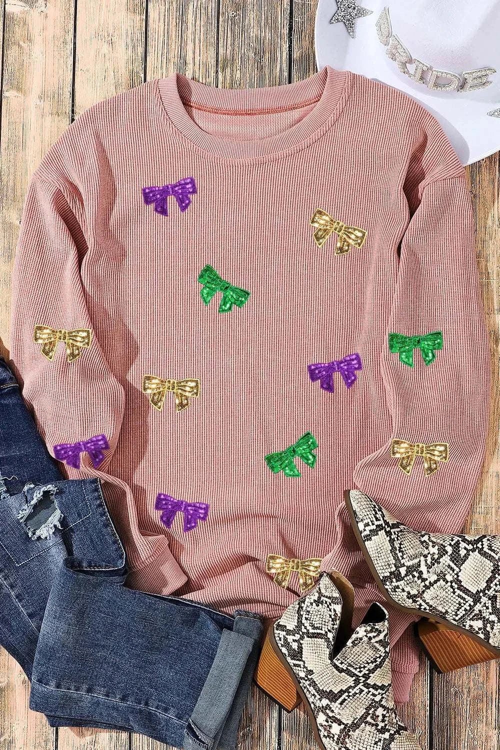 Pink round neck sweatshirt with colorful sequin bow decorations, styled with denim jeans and snake print boots.