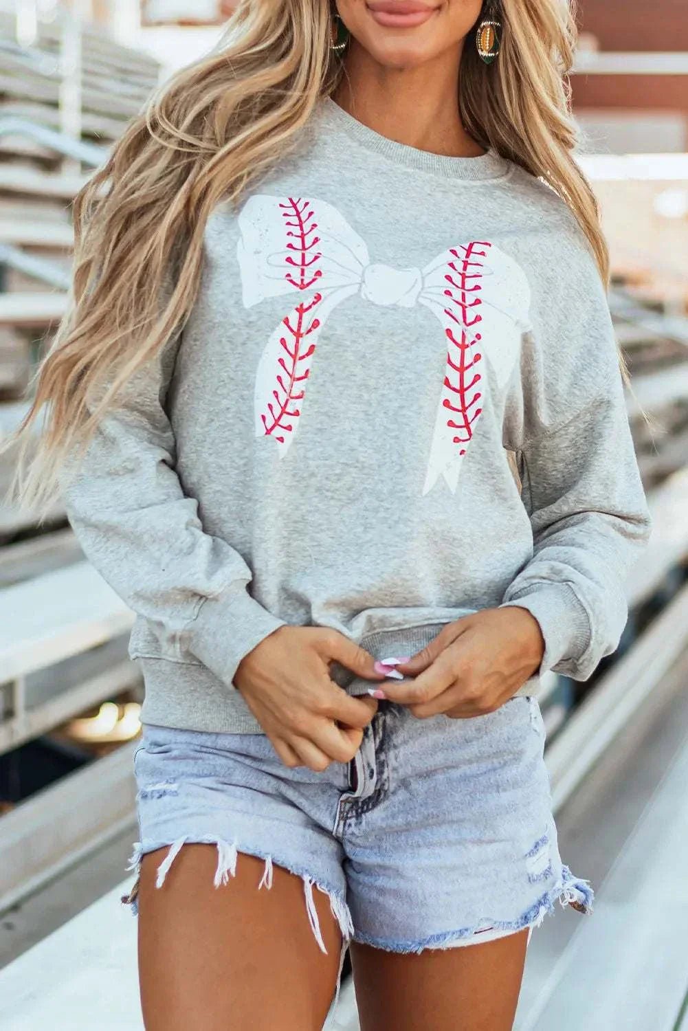 Bow graphic round neck long sleeve sweatshirt in gray with baseball stitch design, worn by model.