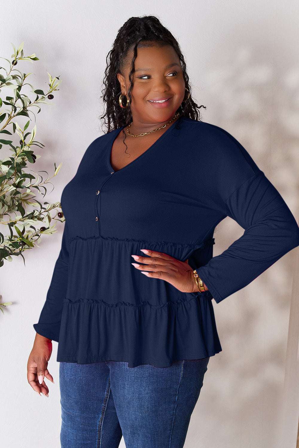 Navy blue half button long sleeve blouse with ruffle hem, worn by smiling model.