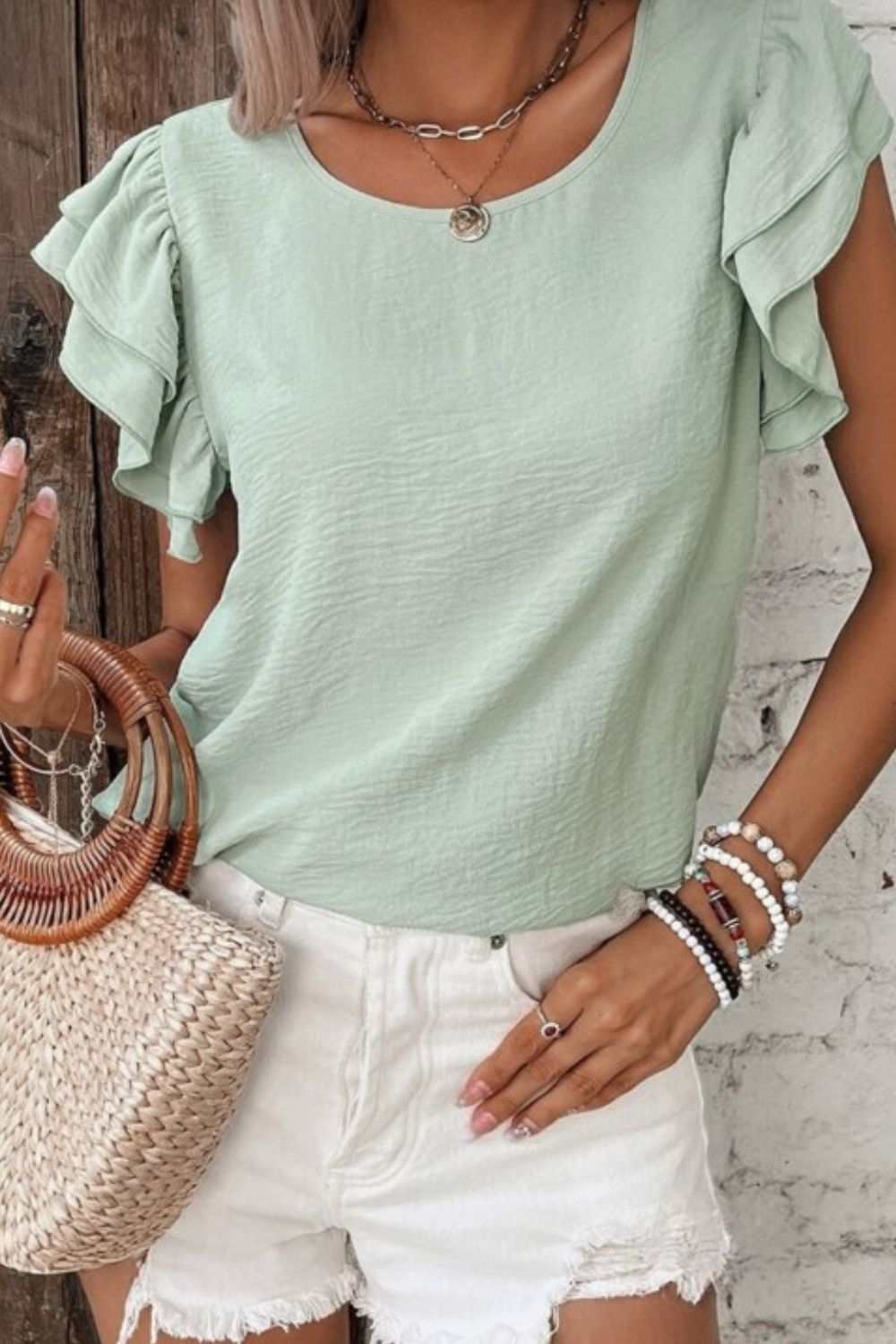 V-Neck ruffled cap sleeve blouse in light green, paired with white shorts and a straw purse.