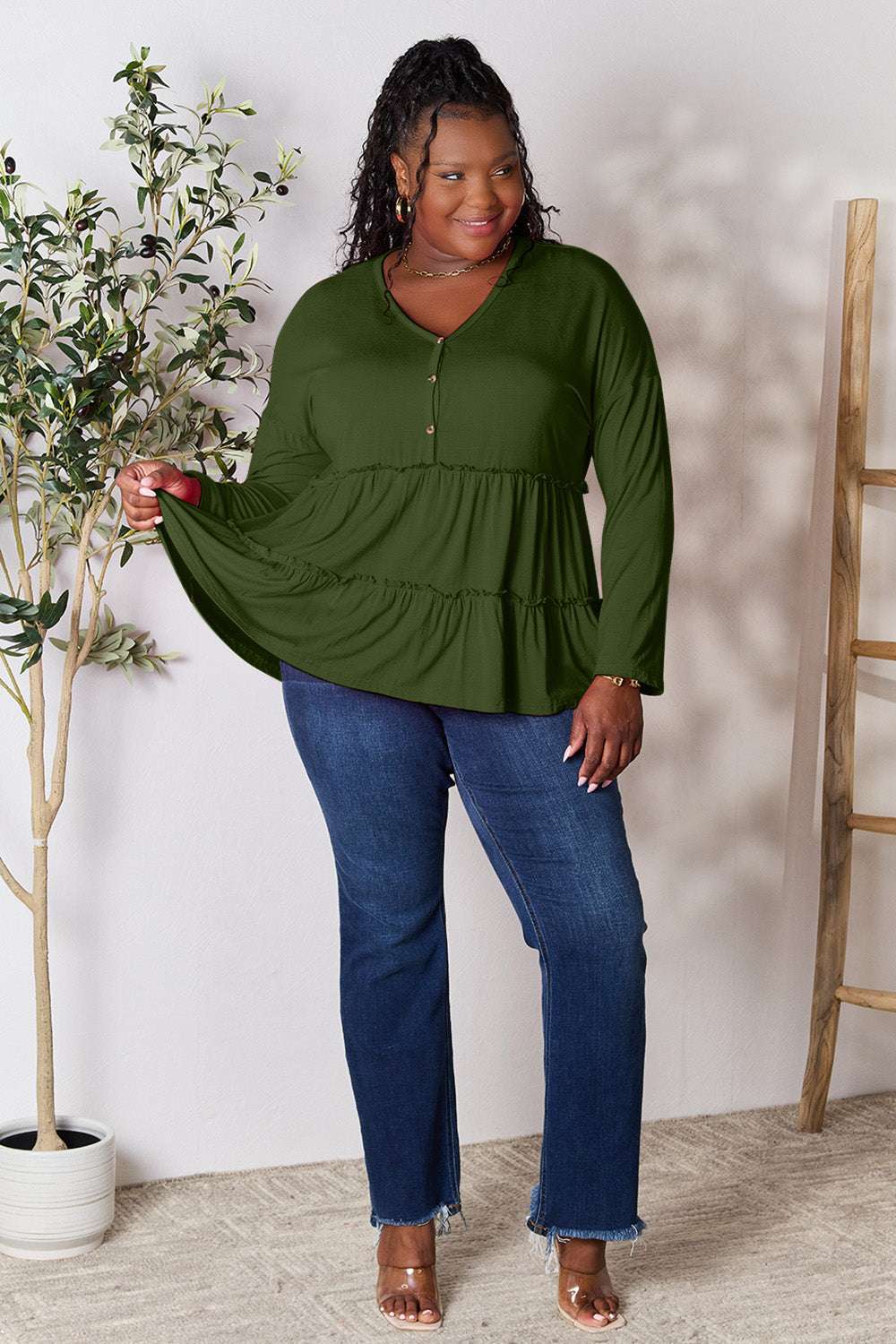 Half button long sleeve ruffle hem blouse in green, paired with jeans.