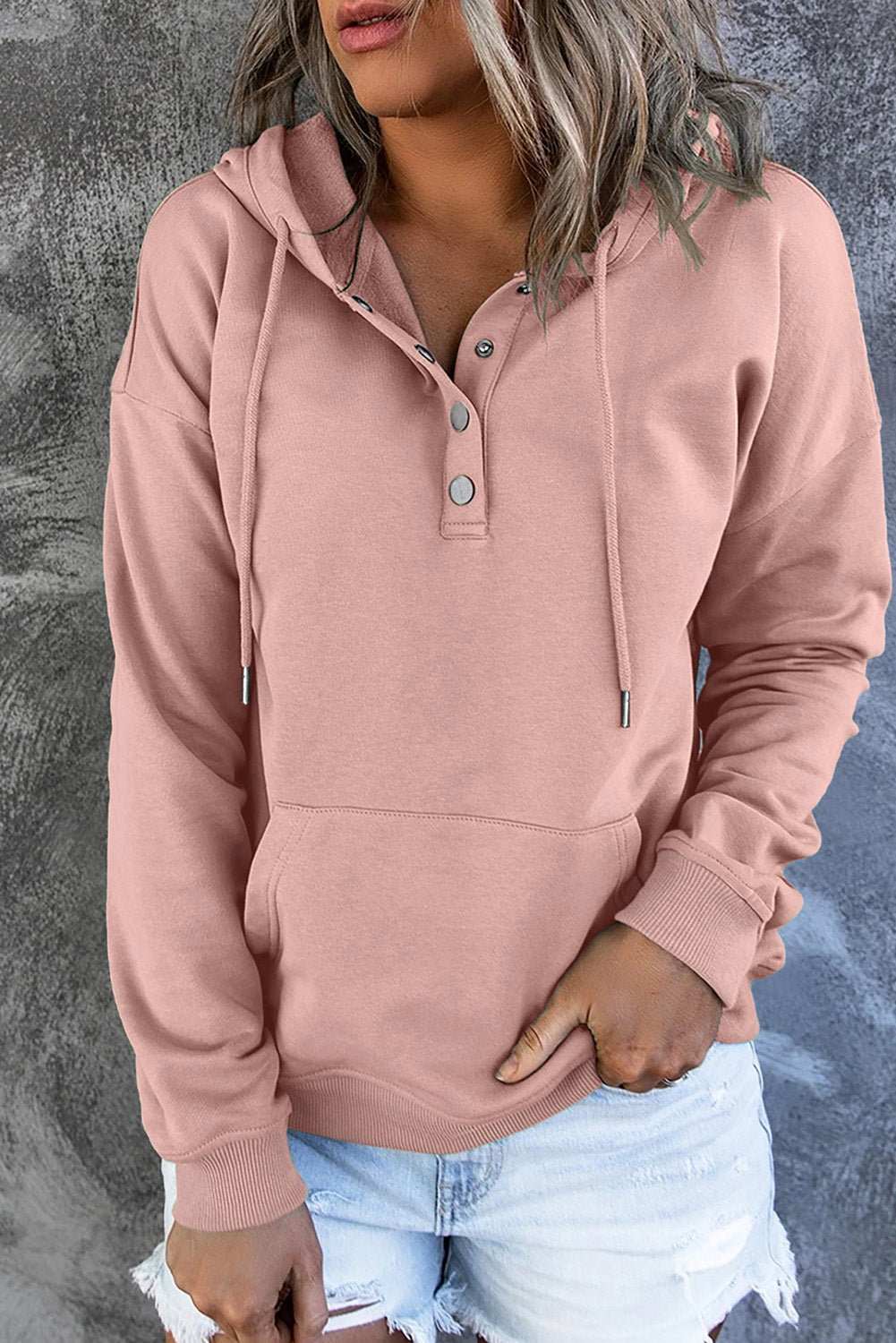 Pink dropped shoulder long sleeve hoodie with front pocket and buttoned neckline worn with distressed denim shorts