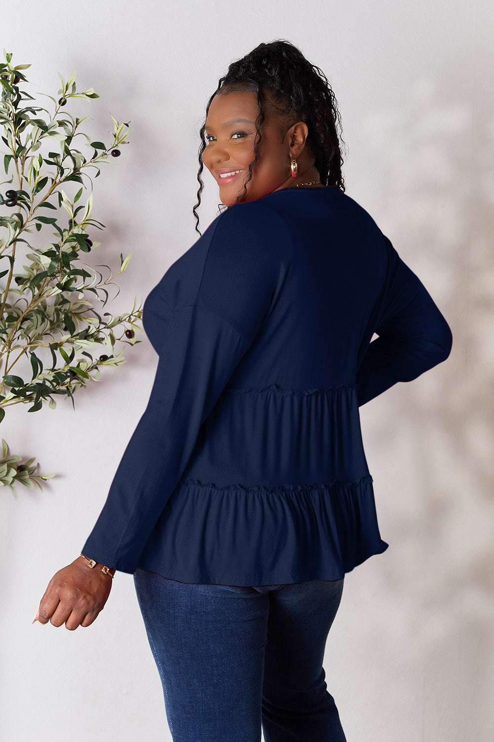 Curve model wearing a navy Half Button Long Sleeve Ruffle Hem Blouse, showcasing back ruffle detail.