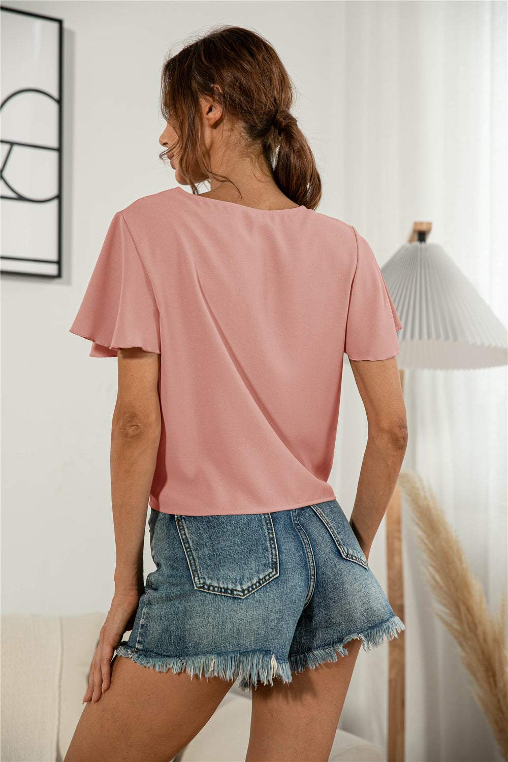 Decorative button V-neck tied blouse with short flutter sleeves in a solid pink color, styled casually.