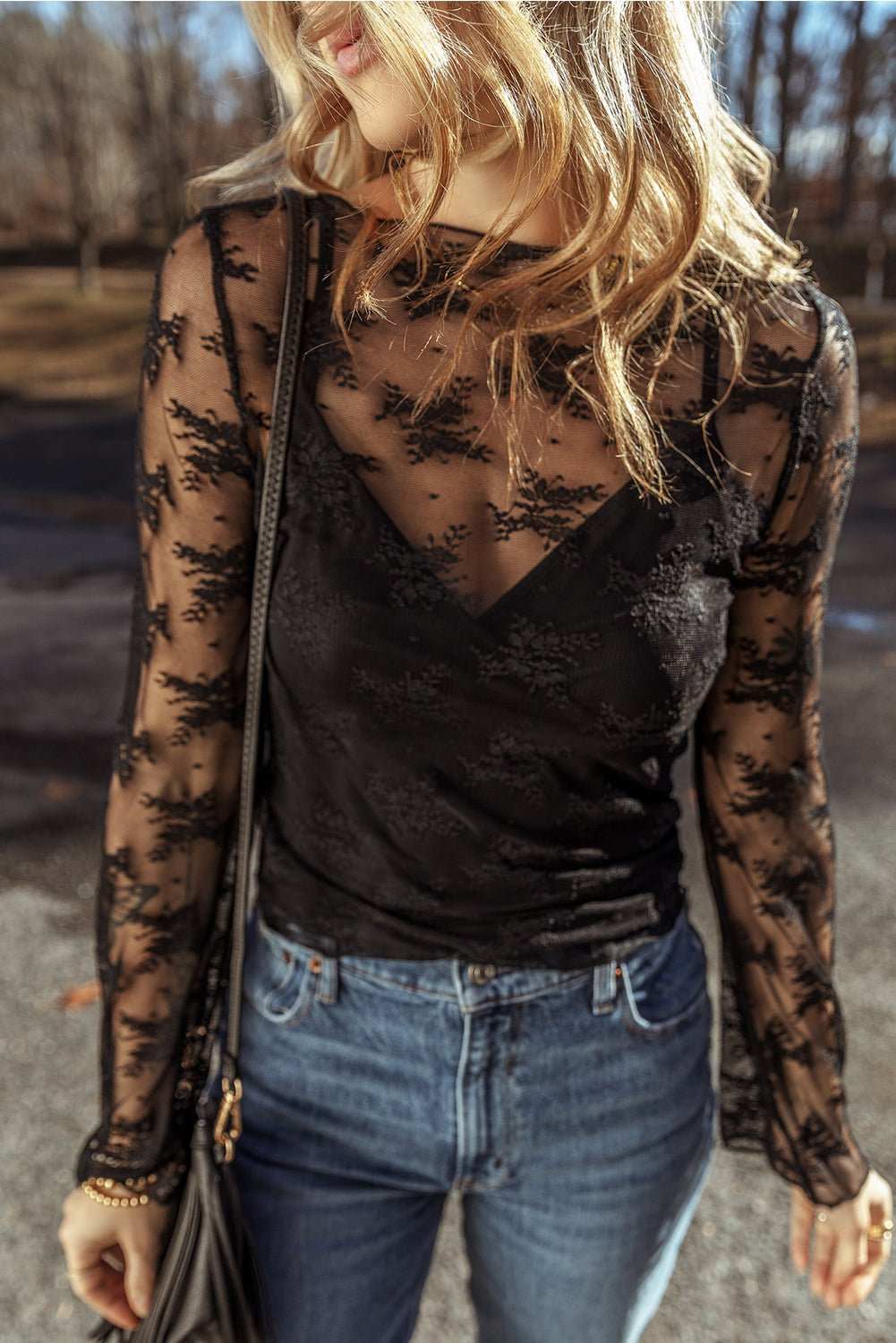 Woman wearing black lace mesh crochet slim fit long sleeve blouse with crew neck paired with blue jeans outdoors