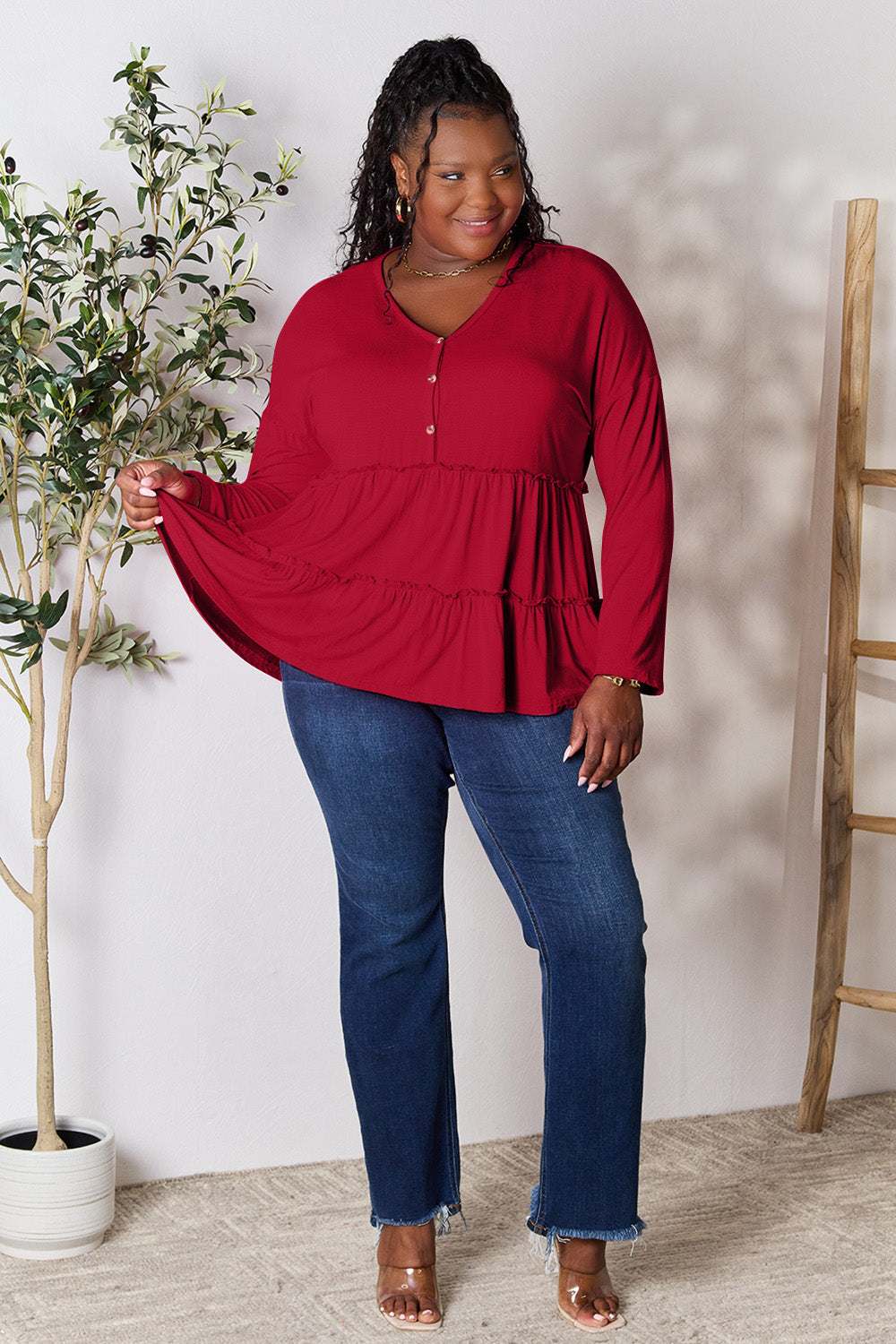 Red half button long sleeve ruffle hem blouse worn by model with jeans, featuring a flattering layered design.