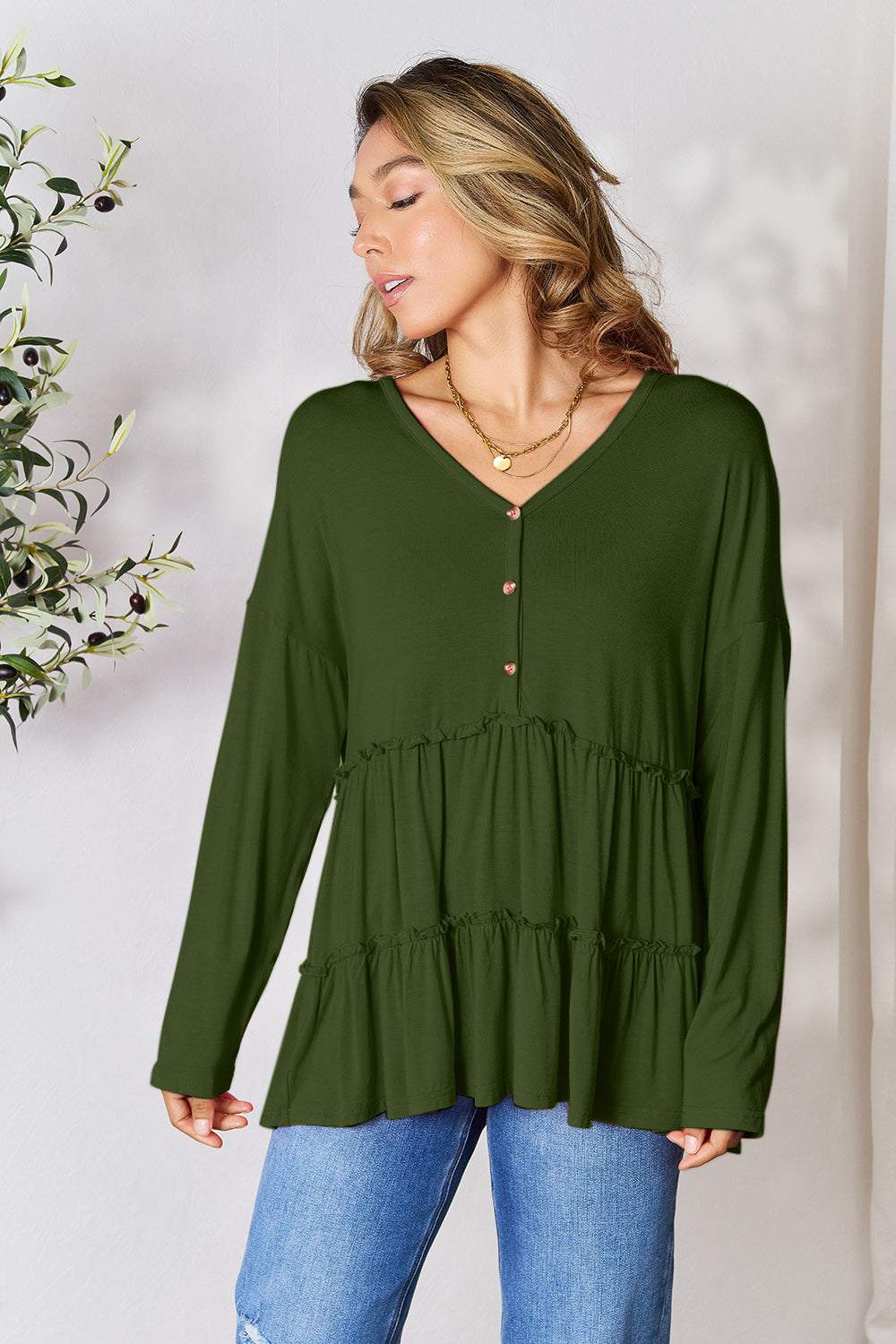 Half button long sleeve ruffle hem blouse in green on model.