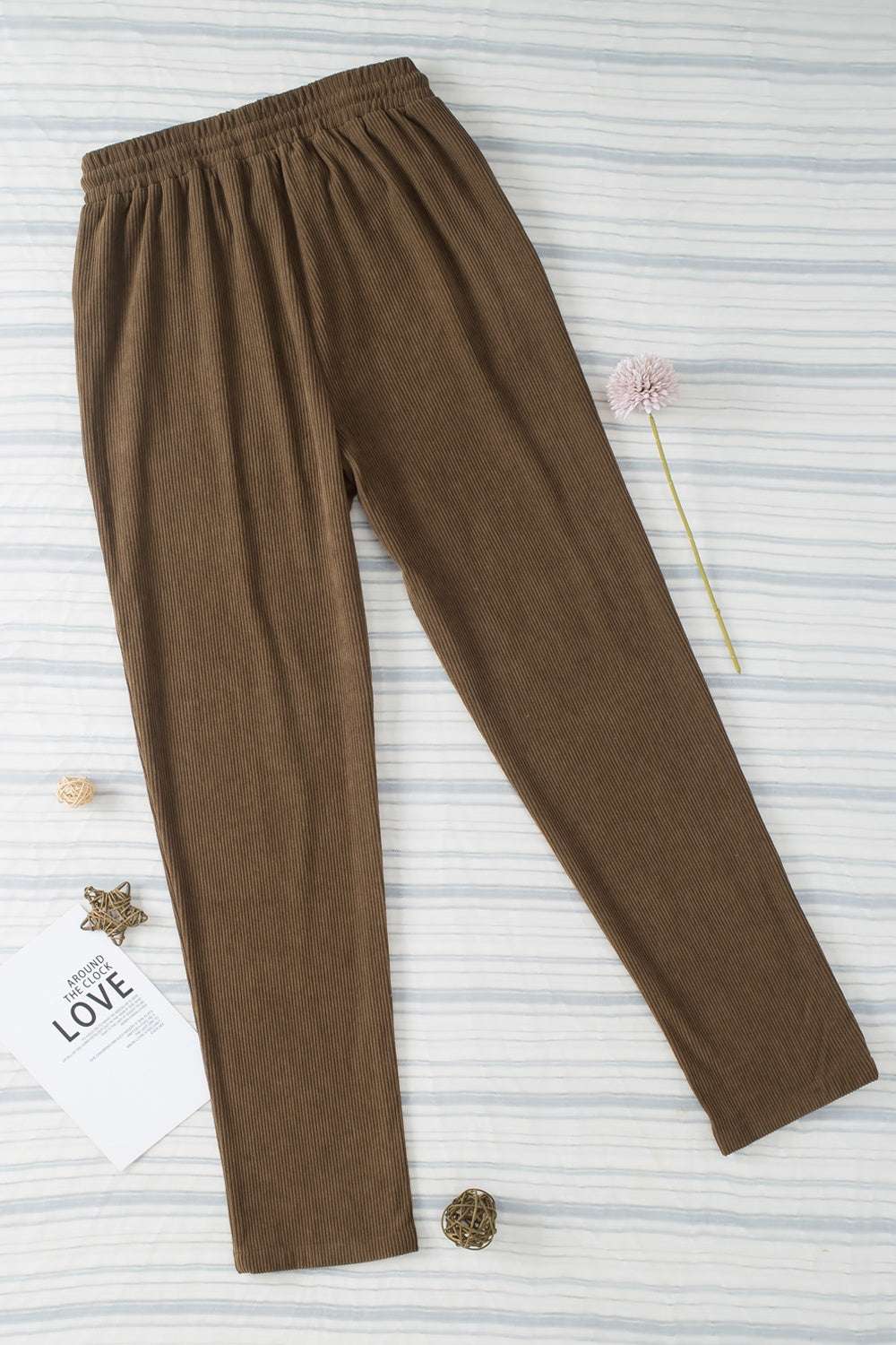 Brown drawstring straight pants with pockets on striped background.