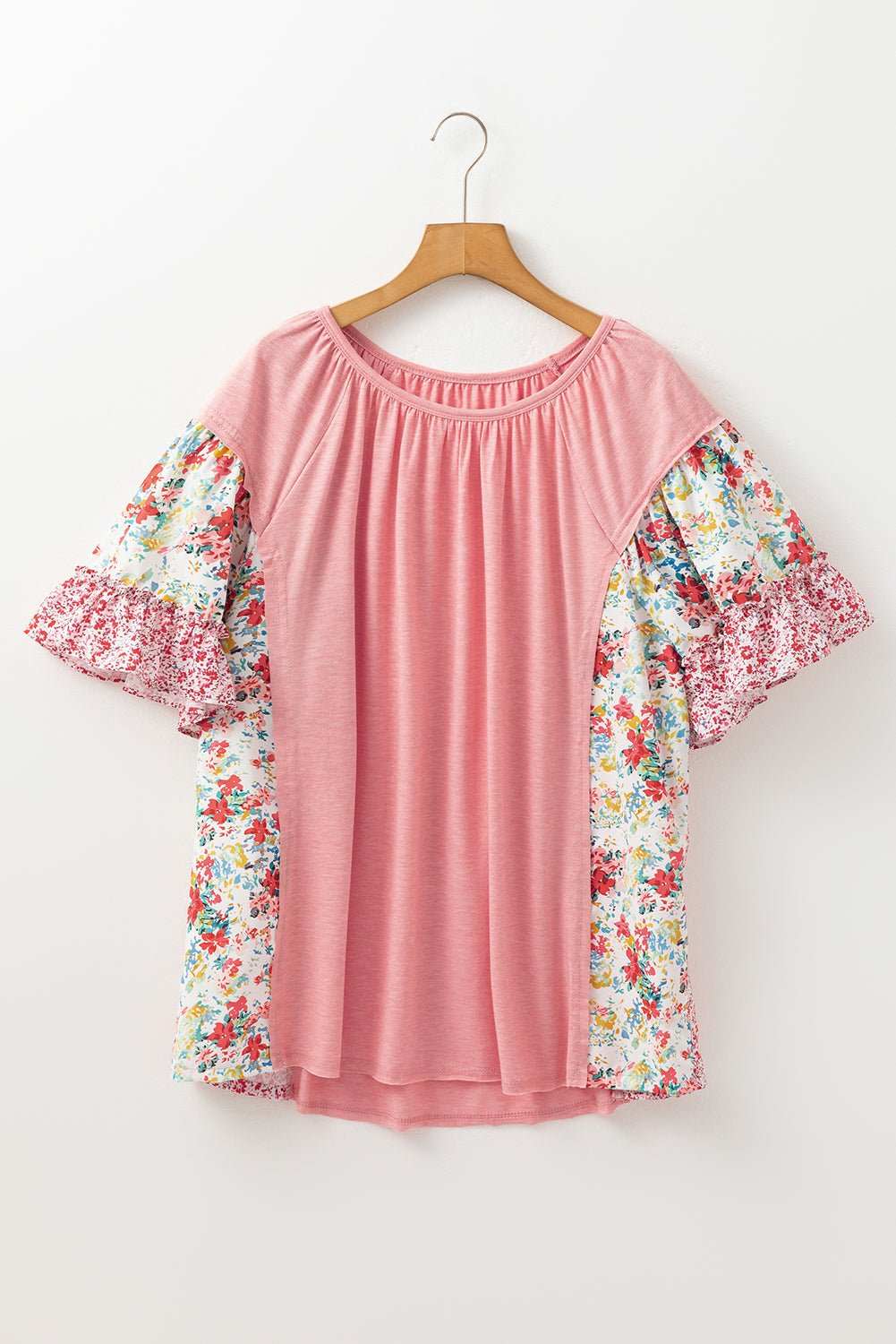 Pink plus size blouse with floral patchwork and ruffled short sleeves on wooden hanger against white background