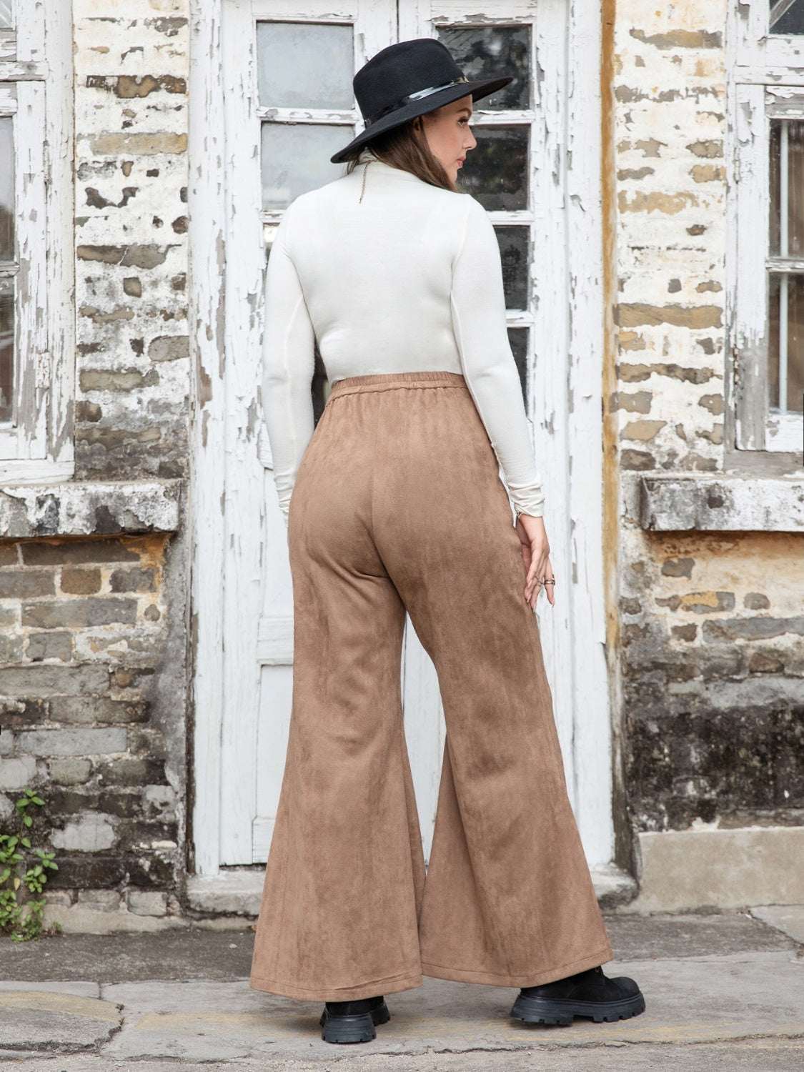 Plus size pocketed flare pants in brown, worn by a model in a white top and black hat, showcasing a stylish back view.