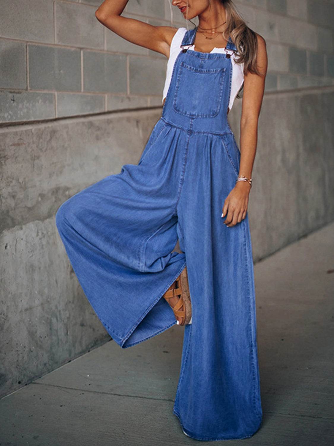 Woman wearing wide leg denim overalls with basic style and no stretch, styled with a white tank top and sandals.