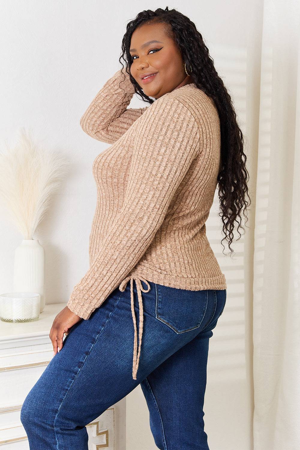 Curve model wearing a drawstring ribbed long sleeve t-shirt in beige, paired with blue jeans.
