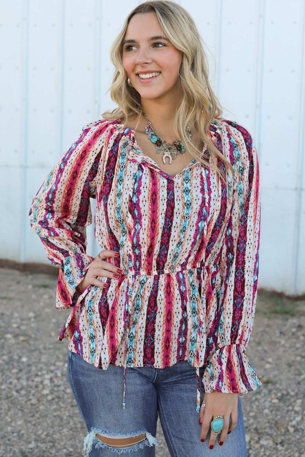 Woman wearing multicolour western print split neck peplum blouse with long sleeves and jeans outdoors