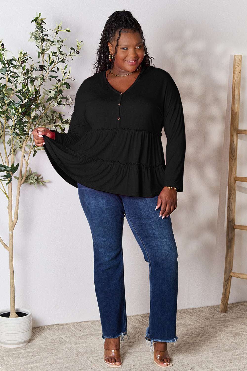 Black half button long sleeve blouse with ruffle hem, worn by model with jeans.