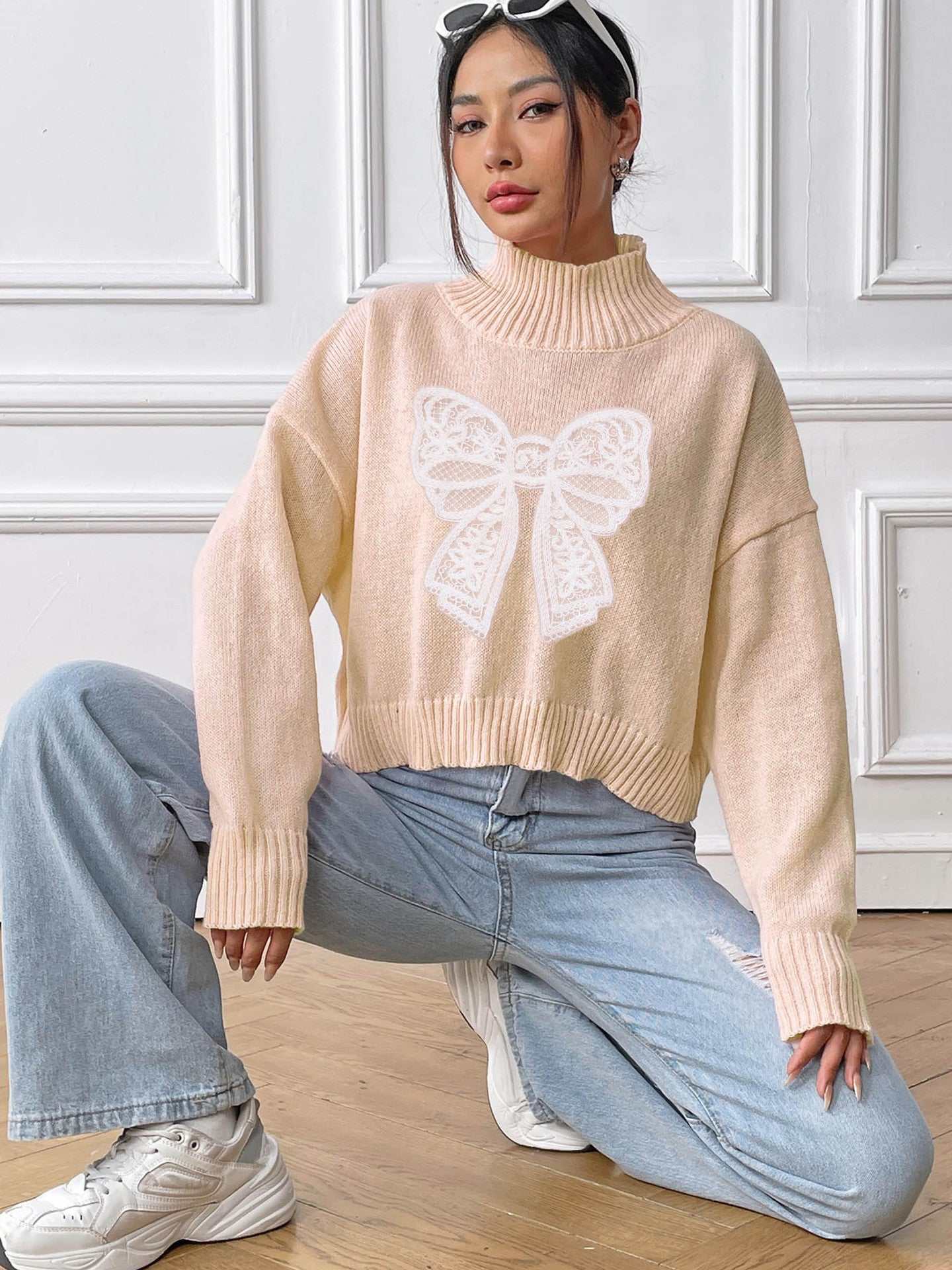 Bow Turtleneck Long Sleeve Sweater in light beige with a decorative bow design on the front, worn with light blue jeans.