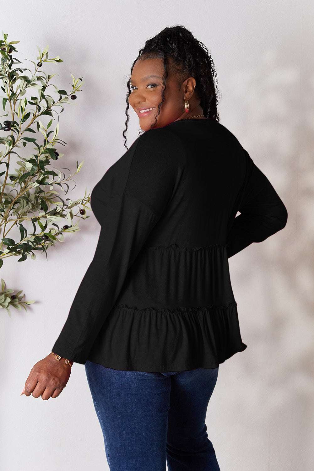 Half button long sleeve ruffle hem blouse in black, worn by model, showing back detail.