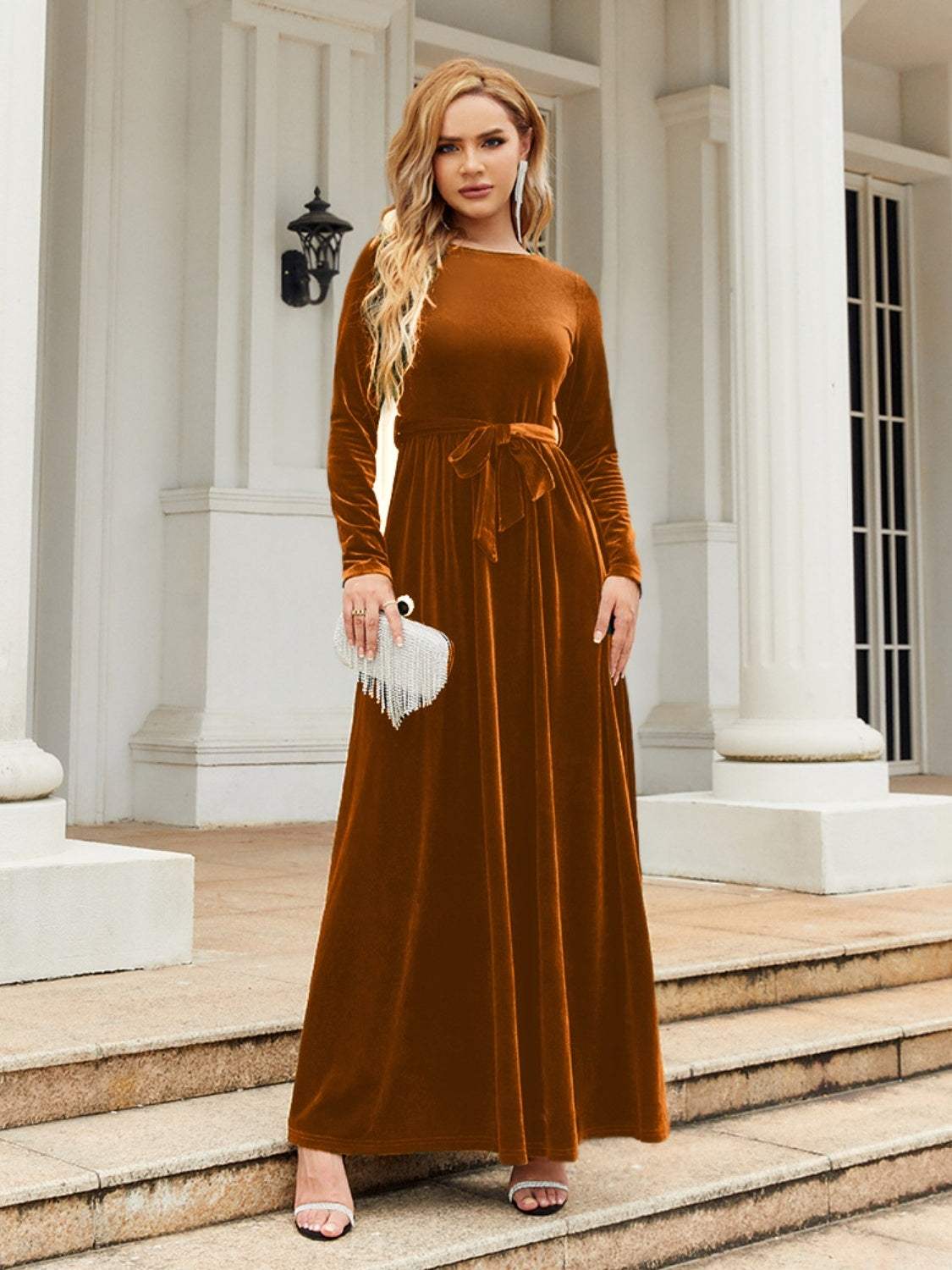 Tie Front Round Neck Long Sleeve Maxi Dress in rust, worn by model standing outside, elegant and opaque with slight stretch.