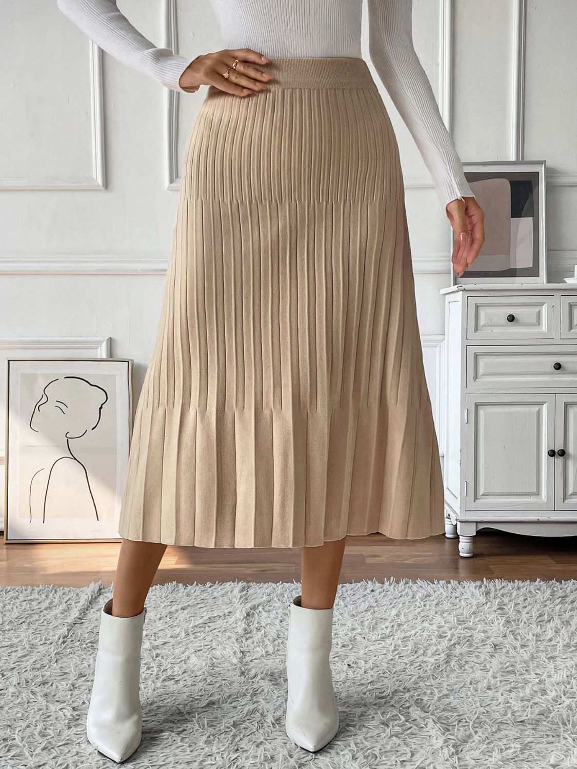 Beige pleated midi sweater skirt with a basic style, worn with white boots.