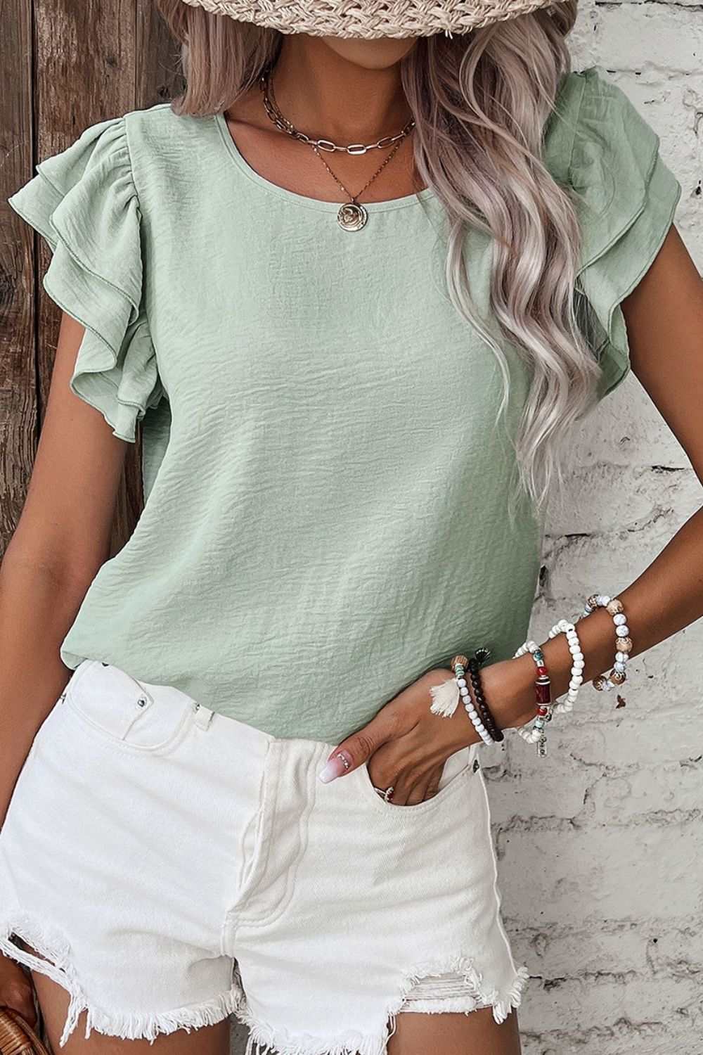 V-Neck ruffled cap sleeve blouse in light green, worn with white shorts.