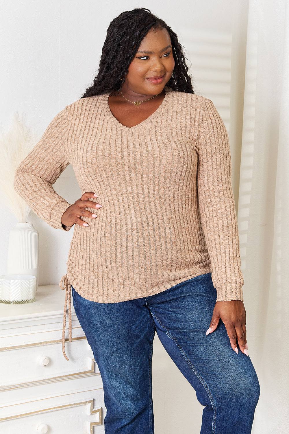Curvy model wearing beige drawstring ribbed long sleeve T-shirt with blue jeans.