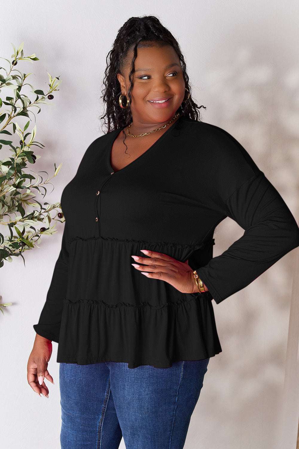 Black half button long sleeve ruffle hem blouse worn by a smiling model with curly hair and hoop earrings.