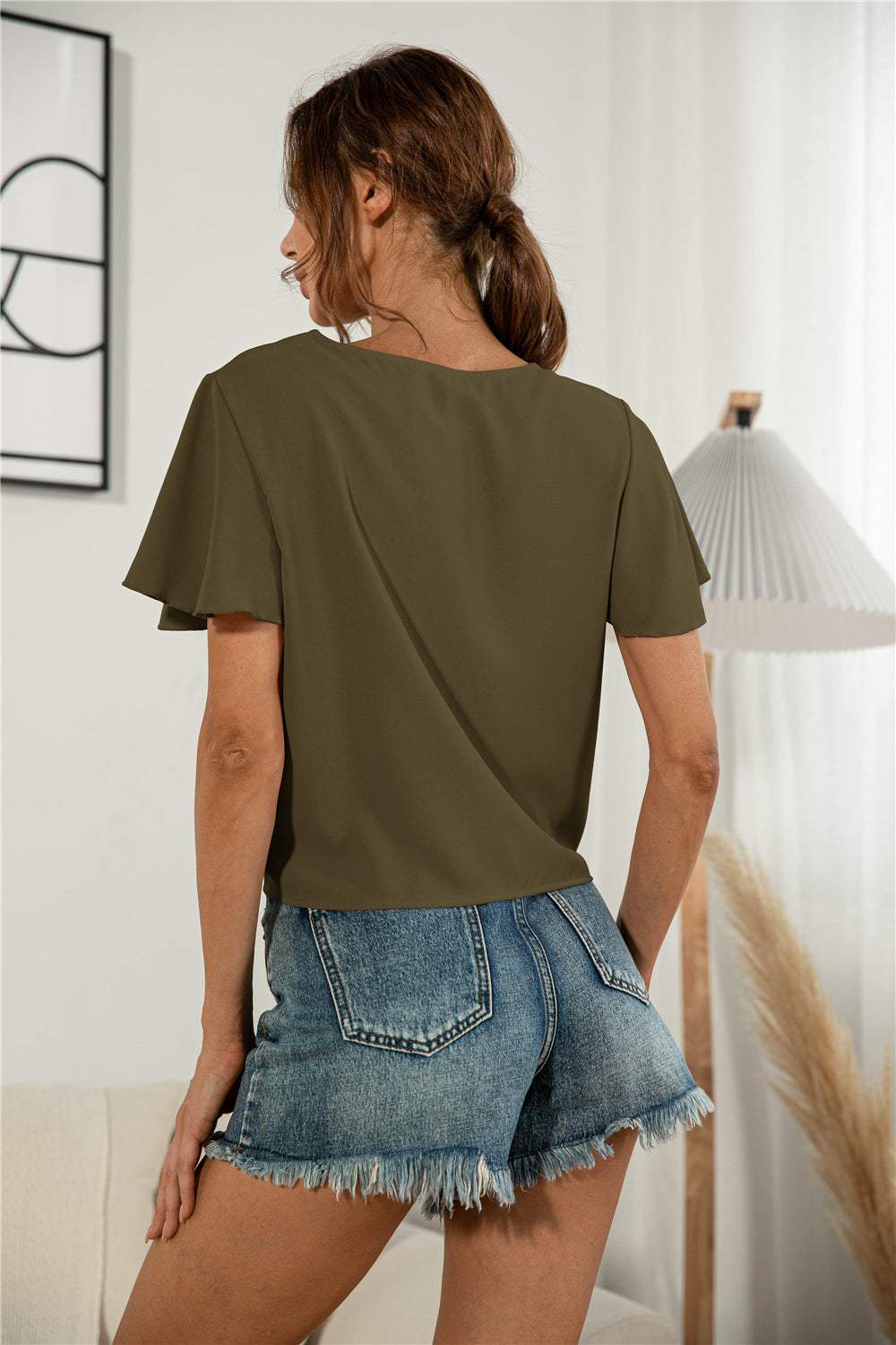 Decorative button V-neck tied blouse in solid color with flutter sleeves, styled casually with denim shorts.