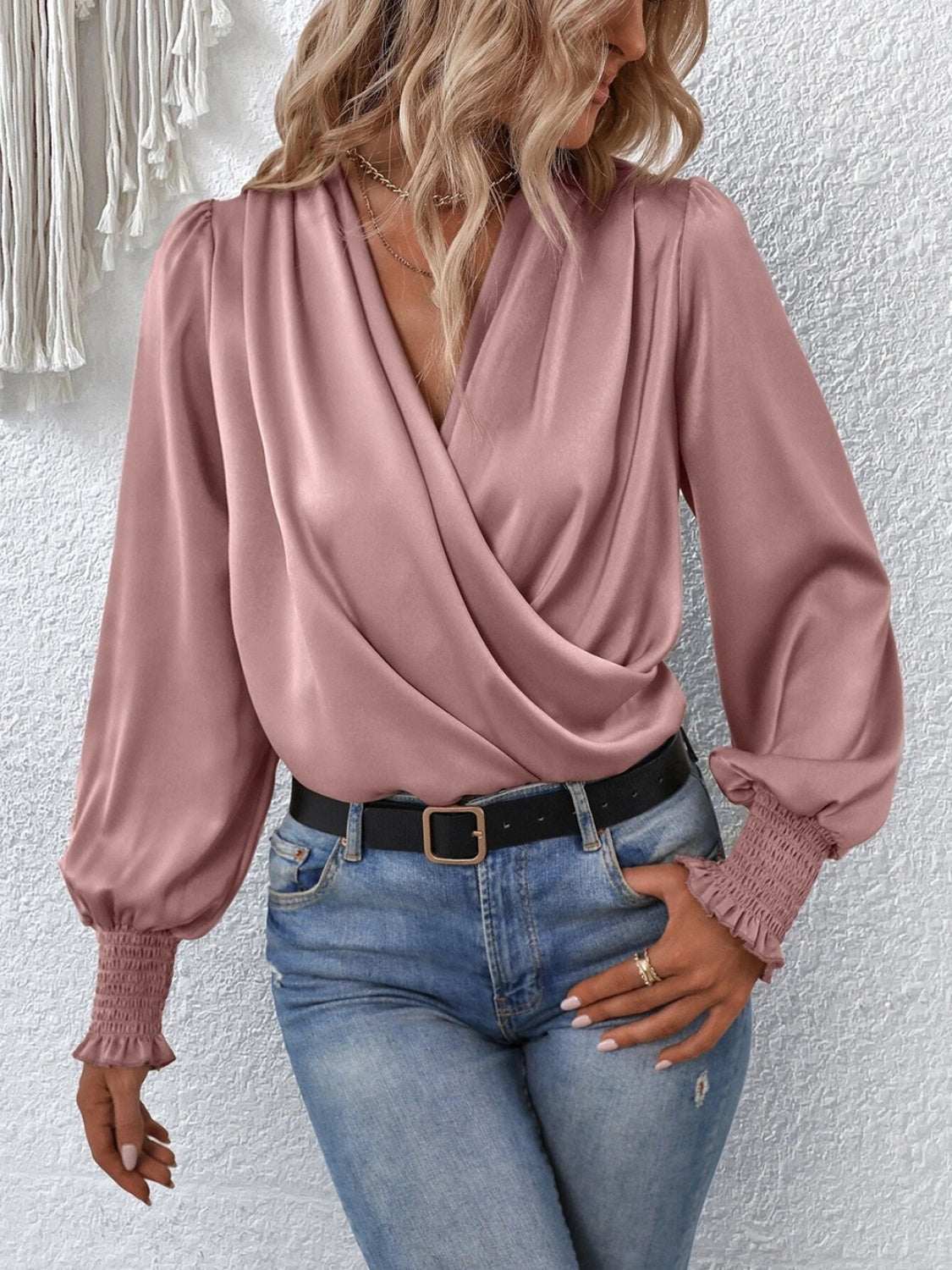 Surplice smocked lantern sleeve blouse in pink worn by woman with jeans.