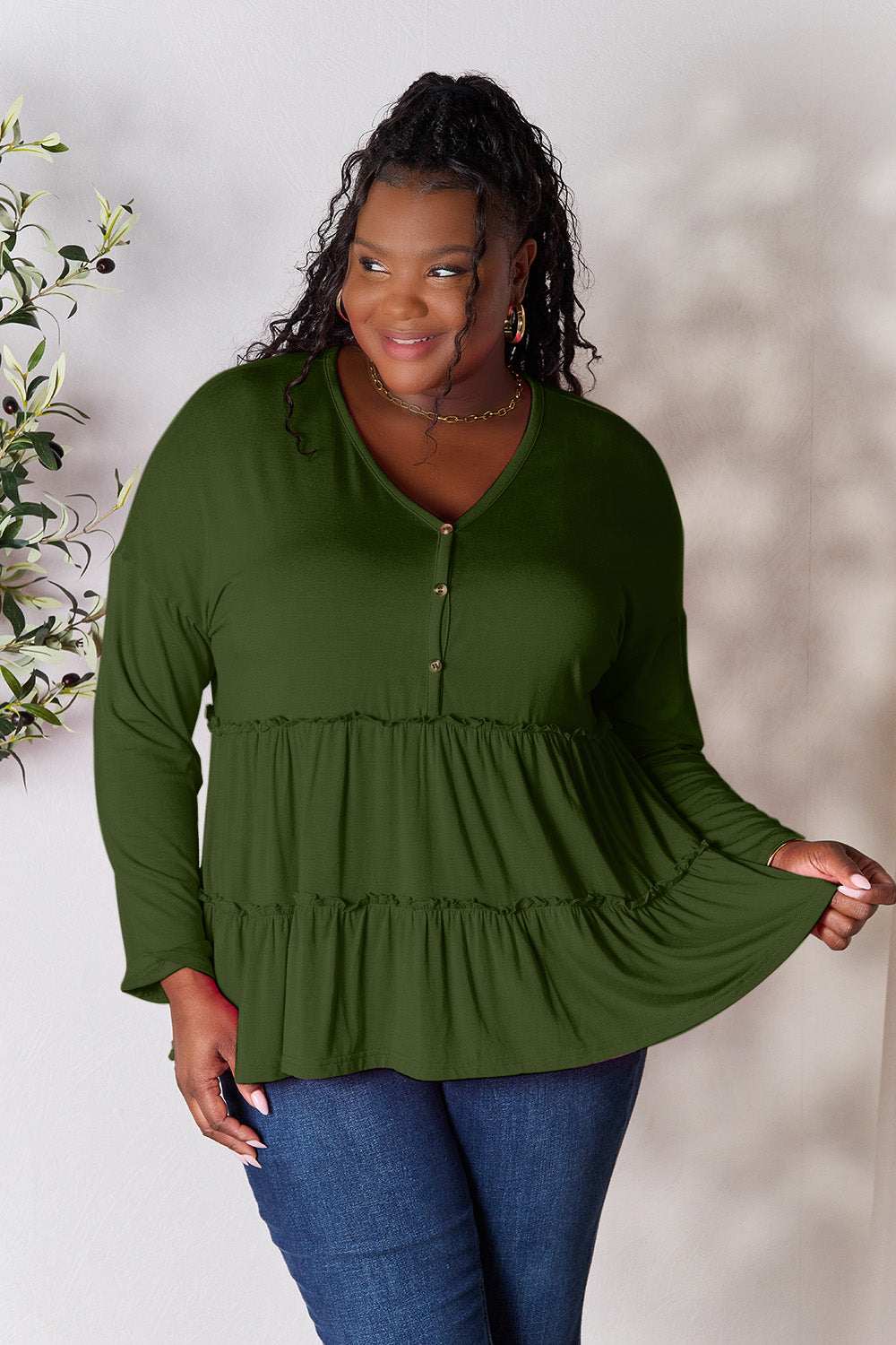 Curve model wearing green half button long sleeve ruffle hem blouse, paired with jeans.