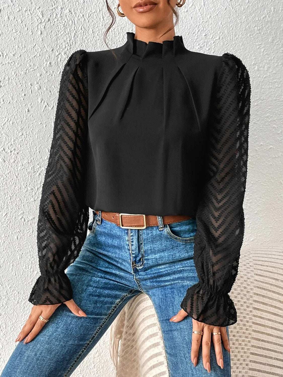 Woman wearing black mock neck flounce sleeve blouse with ruffled, semi-sheer sleeves, paired with blue jeans.